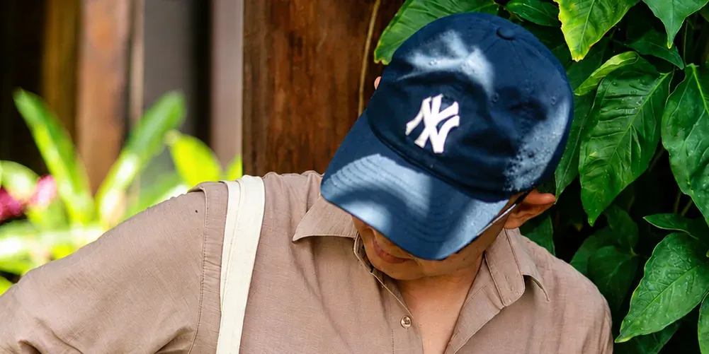 Andriyan Febriyanto in a blue cap and linen shirt, smiling and looking down among tropical green leaves